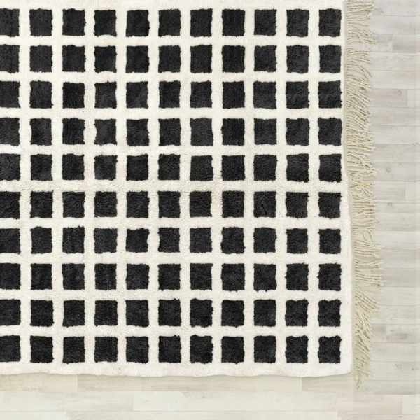 A black and white Beni Ourain rug featuring a bold grid pattern, handwoven with 100% natural wool, displayed on a wooden floor